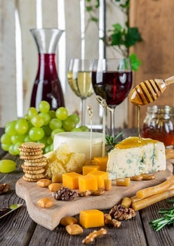 Picture of mix different cheese plate serve with green grapes.  Wine glasses with white and red wine 